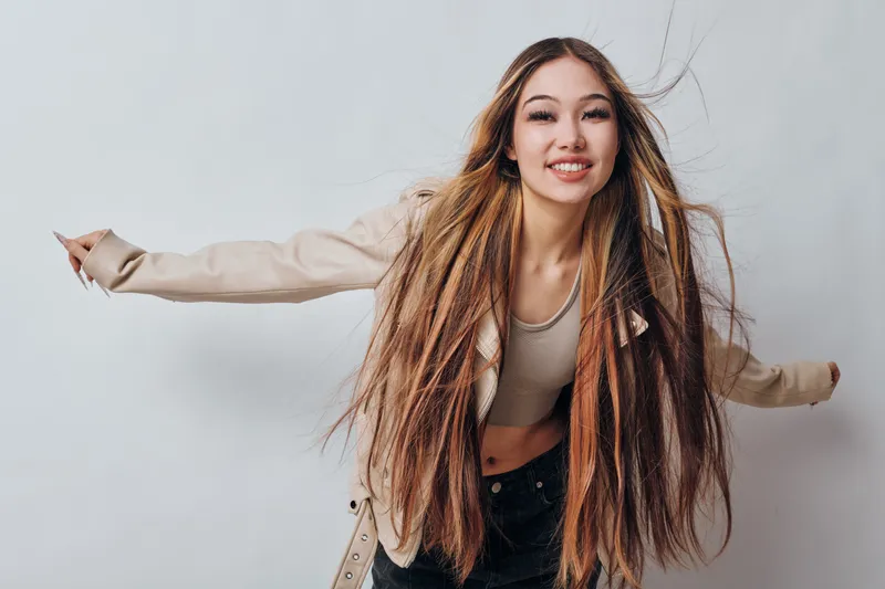 Young woman with long braided hair and casual clothes smiling and posing with arms outstretched on white background in studio. Fashion, beauty and happiness concept.