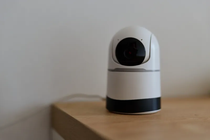 Close-up of a home security camera on a wooden table, highlighting a sleek white body and black lens, conveying safety, privacy awareness, and contemporary technology.