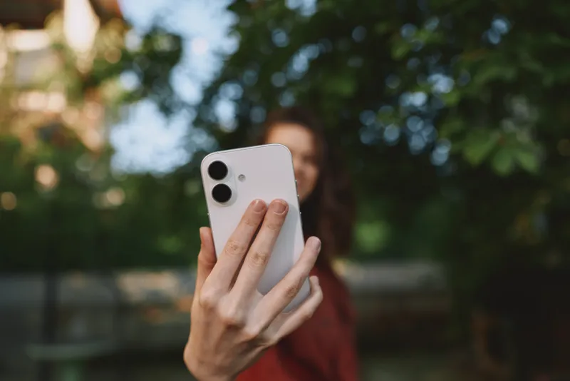 Selfie focused woman outdoors, lifestyle portrait with smartphone, candid moment amid greenery, showcasing casual fashion and natural light, lively vibe throughout today