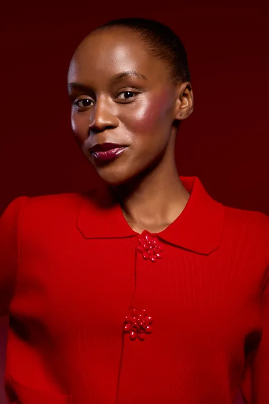 Portrait of a young black woman with dark skin wearing a red sweater with decorative buttons. She poses confidently against a dark red background. Concept of fashion and elegance.