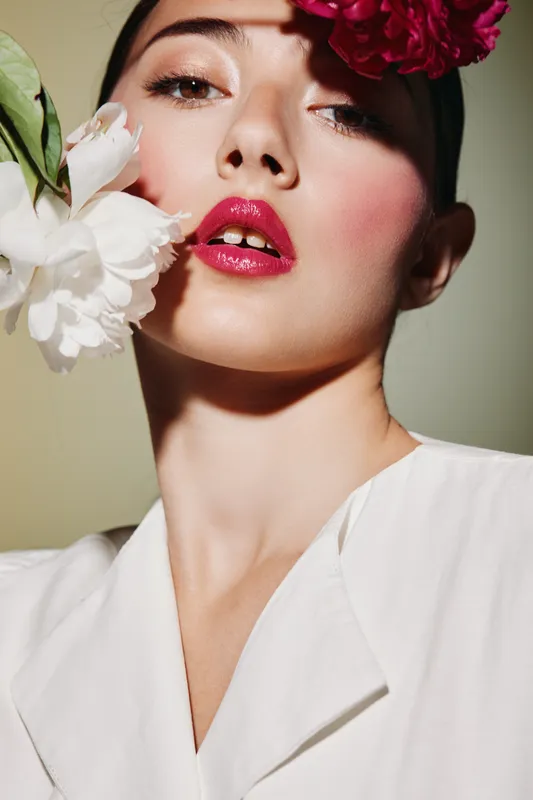 Close-up of a creative beauty model with vivid pink lips and floral accessories in soft light. Artistic fashion portrait emphasizing makeup and fresh skin.