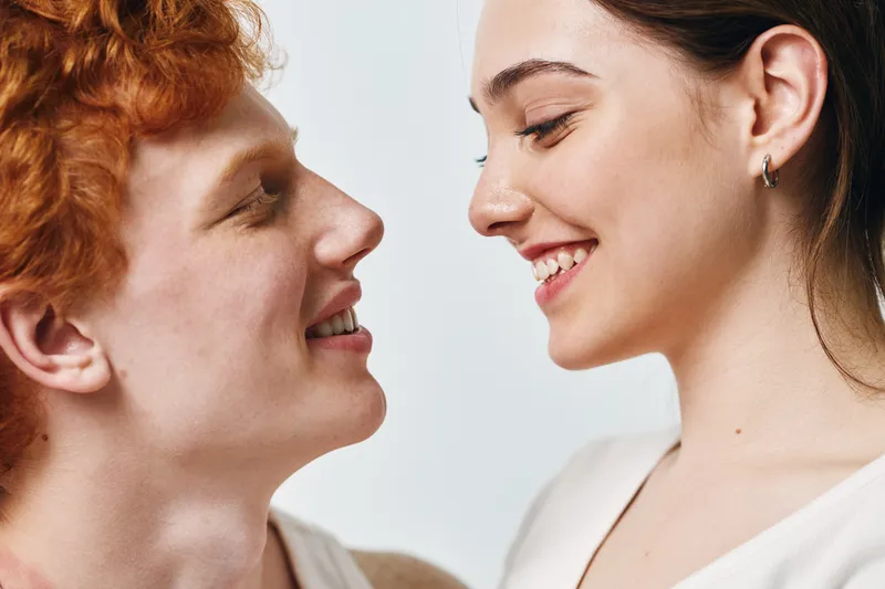 Young couple smiling and looking at each other with happiness and affection closeup portrait of man and woman with light background in love and relationship moment.