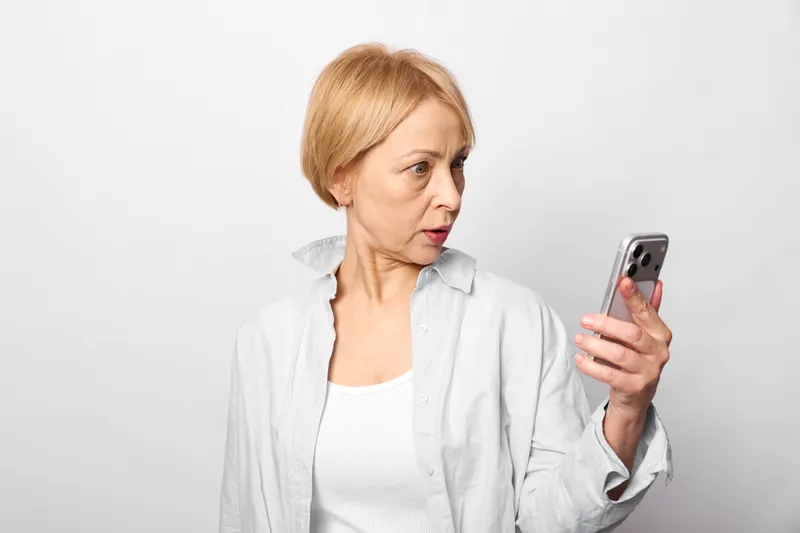 Elderly woman smartphone technology portrait studio communication senior modern internet theme. Holding a mobile phone, she looks thoughtful on a clean white background.