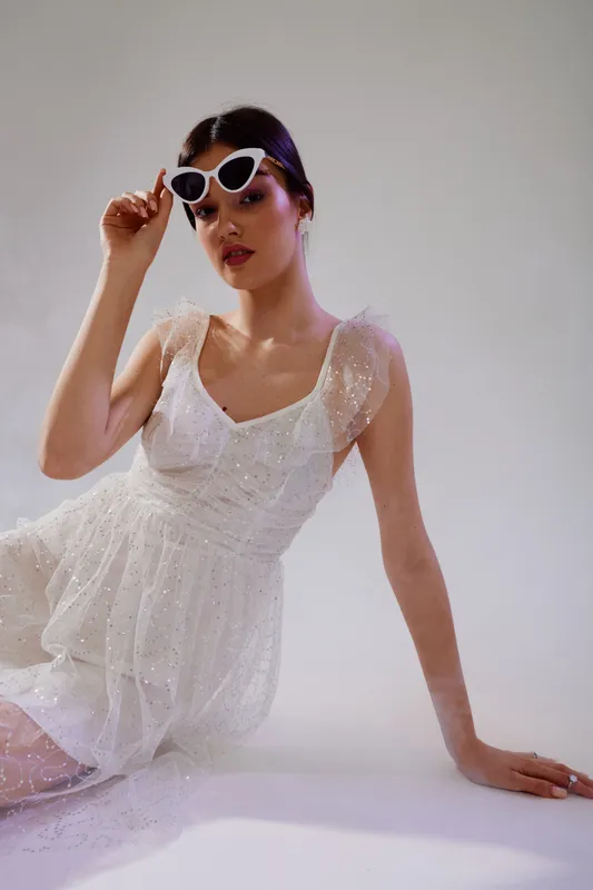 Young woman in a white dress and stylish sunglasses poses elegantly on a light background. Concept of beauty, fashion, and modern style with soft lighting.