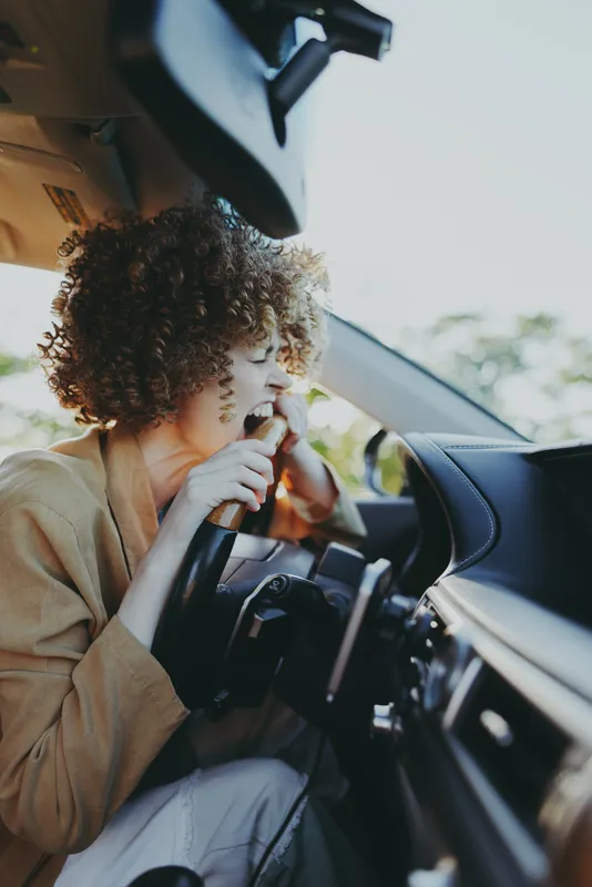 Woman driver in car interior, lifestyle shot with retro film color, smoking softly, curly hair, warm light, candid moment on the road, relaxed urban mood