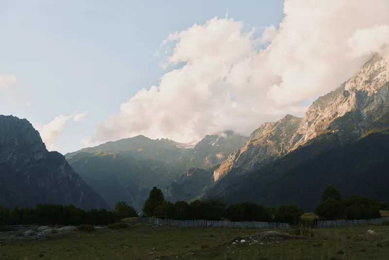 Mountain landscape with rocky peaks and green forest under cloudy sky, natural scenery, outdoor environment, peaceful atmosphere, daylight, wide view