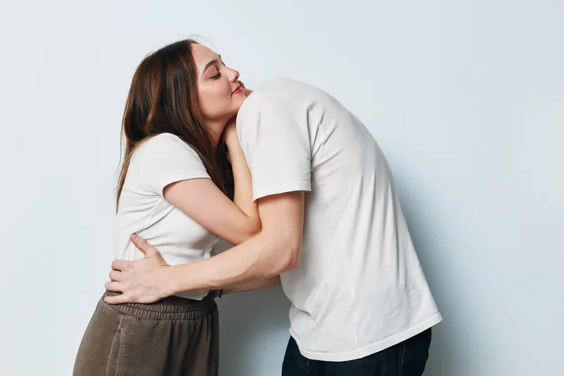 Couple embracing and hugging each other with eyes closed in casual clothing on white background. Young man and woman showing affection and love in studio.