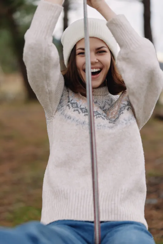 Joyful girl on a swing in a park, wearing a cozy knitted sweater and beanie, smiling as she enjoys a crisp outdoor moment.