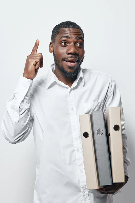 African American man with dark skin holding office folders and pointing up with finger, wearing white shirt, isolated on white background for business concept.