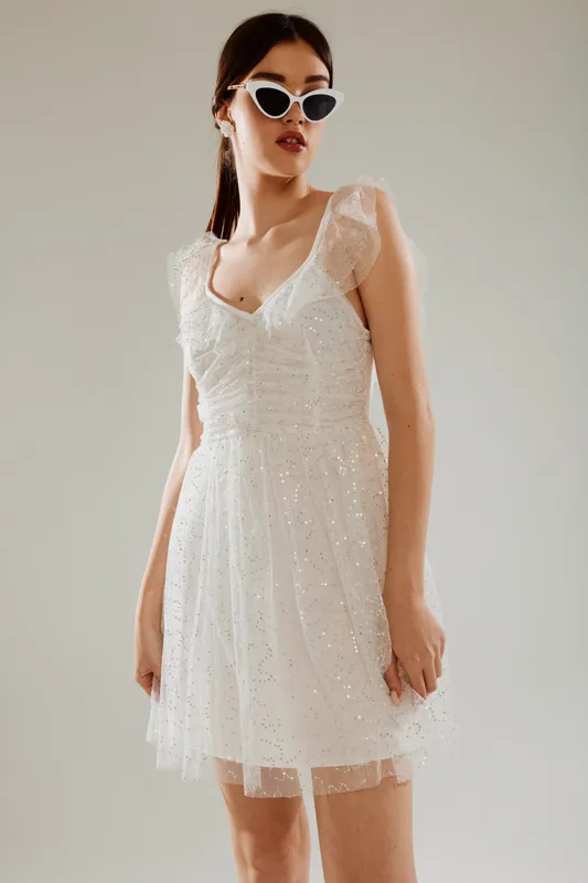 Young woman in a white elegant dress and stylish sunglasses poses confidently against a neutral background. Concept of woman beauty fashion and modern style.