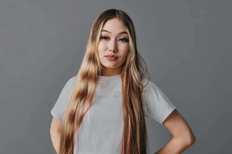 Portrait of confident young woman with long hair in white t shirt standing with hands on hips against grey background studio. Female model expression fashion style