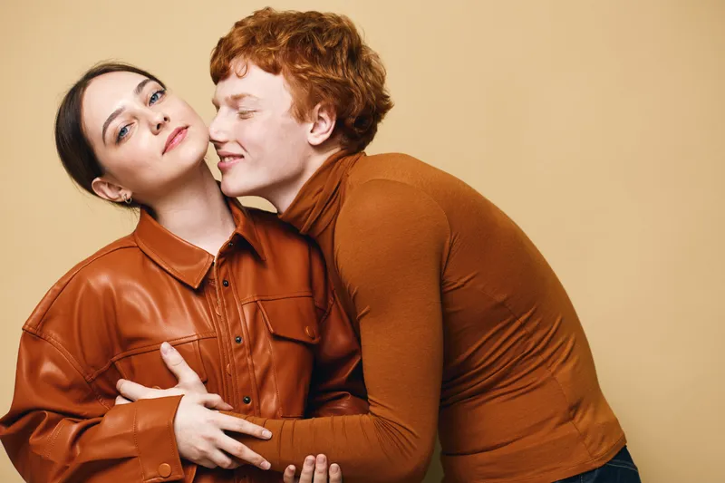 Couple, woman and man embracing in casual autumn clothing with warm brown tones. Young lovers showing affection and closeness in studio, lifestyle portrait with soft light.
