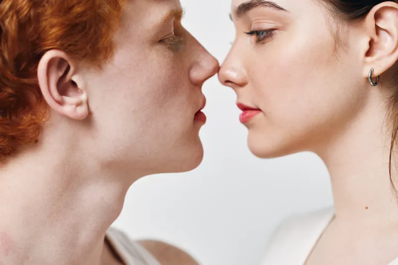 Closeup of young man and woman facing each other with eyes closed for intimacy connection and emotion in studio lighting.
