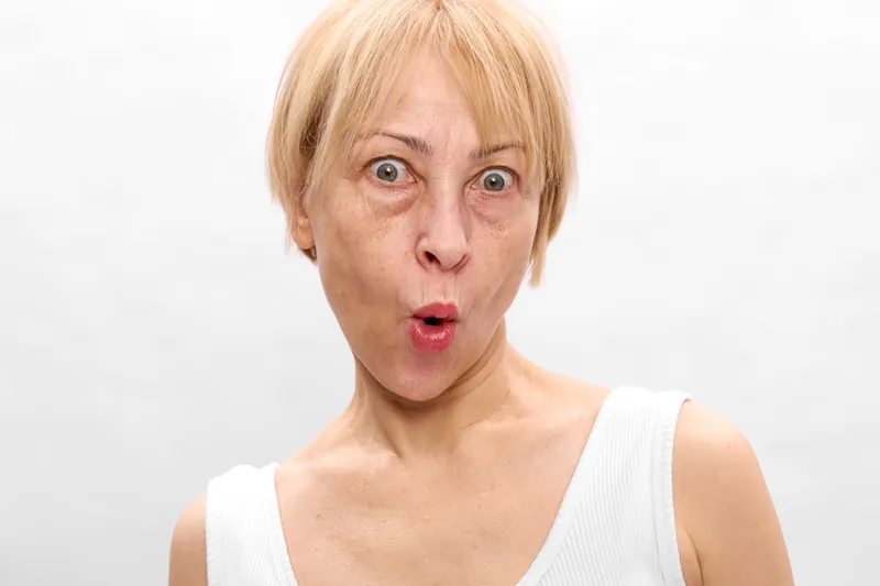 Surprised blond woman portrait with wide eyes and open mouth showing shock and astonishment, emotion and alarm on a clean white studio background, sudden reaction