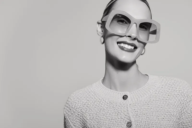 Smiling white woman with fair skin and short hair wearing oversized sunglasses and knitted sweater. Portrait in black and white with positive mood and retro style concept.