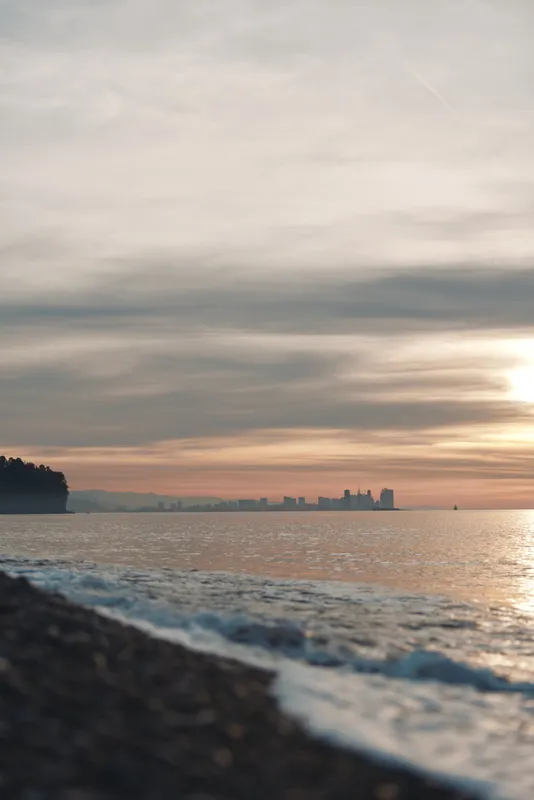 Sea and sunset over a rocky coastline with a calm shoreline and distant skyline on the horizon, reflecting warm light on water for a tranquil coastal scene.