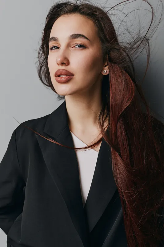 Woman portrait with long hair and natural makeup wearing black coat against gray background. Fashion model with confident expression and stylish look for beauty and style concept.