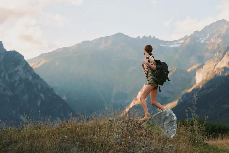 Woman hiking through an alpine meadow with a backpack in a rugged mountain landscape, embracing outdoors travel lifestyle with a focused, serene mood