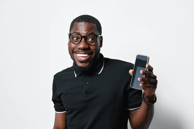 African American man with dark skin and glasses smiling and holding smartphone in hand for communication, technology and social media concept on white background.