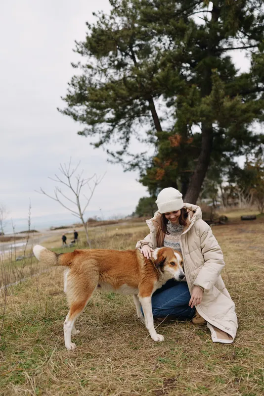 dog woman outdoors companionship park nature autumn a woman crouches beside a dog in an open field sharing a calm moment and mutual trust under a cloudy sky
