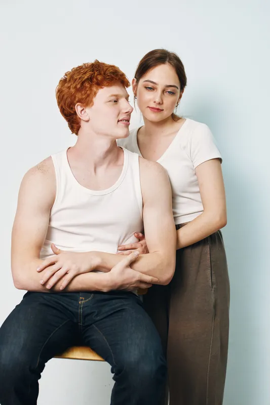 Young couple with red hair and dark hair wearing casual white tops and jeans standing close to each other for love, relationship and affection photo portrait.