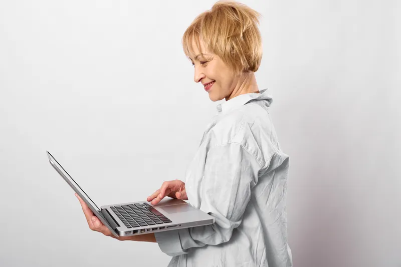 Woman using laptop in studio, side view, focused expression, working and studying, modern technology, productivity, clean white background, soft light