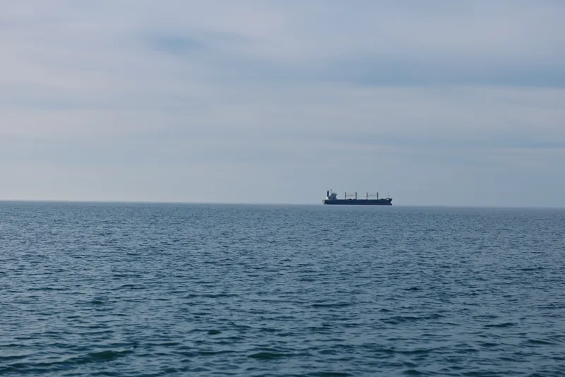 Sea vista with a distant cargo ship on the horizon, calm blue water and cloudy sky, minimalistic maritime scene suitable for business, travel or industry contexts