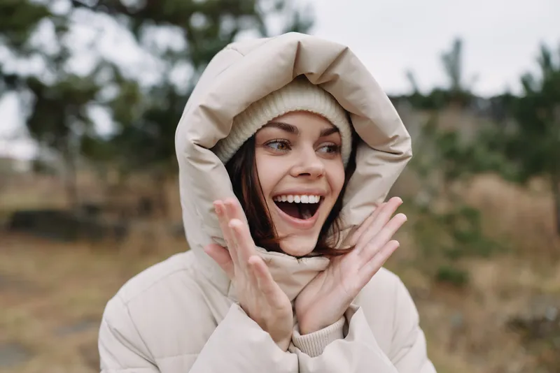 woman outdoor winter happiness with hooded coat in a closeup portrait showing joyful expression and cozy fashion against a windy landscape and natural environment for lifestyle and seasonal stock