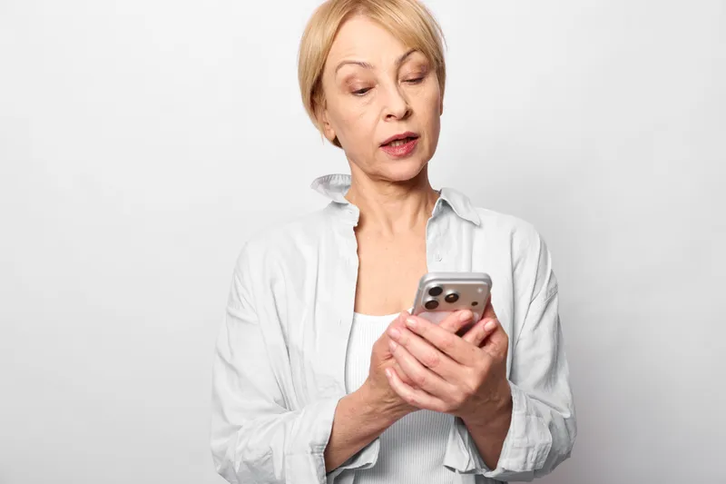 Woman smartphone elderly portrait indoors technology messaging communication, mature woman holds phone, looks concerned, close up on studio white background