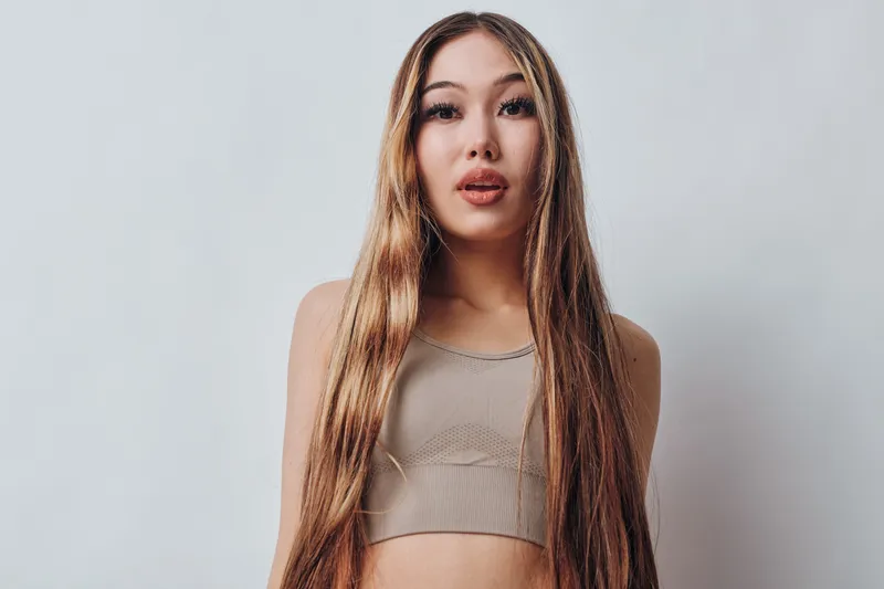 Young woman with long straight hair wearing a crop top posing and looking at camera against plain background indoors with natural expression and casual style.