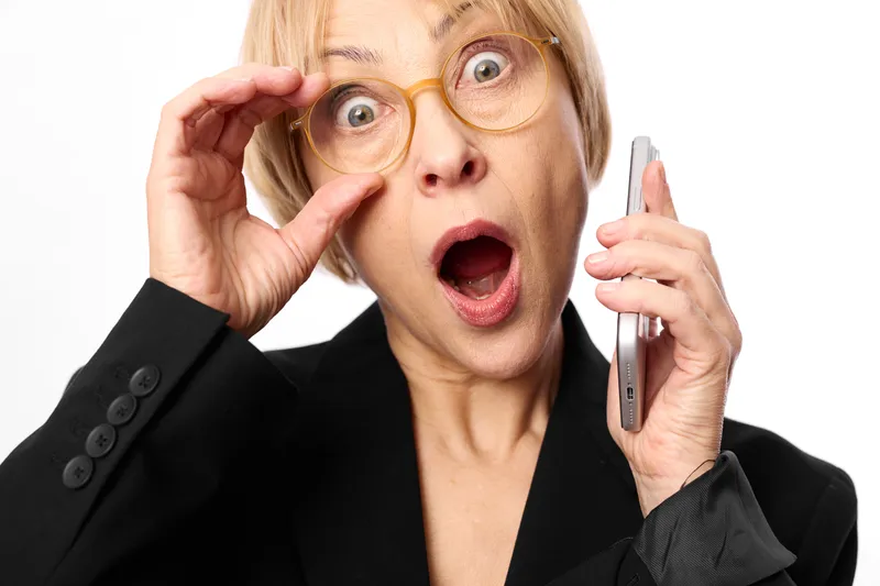 Senior woman, surprised expression, shock moment, holding glasses and phone, communication and technology anxiety, overwhelmed face, close up portrait, white background