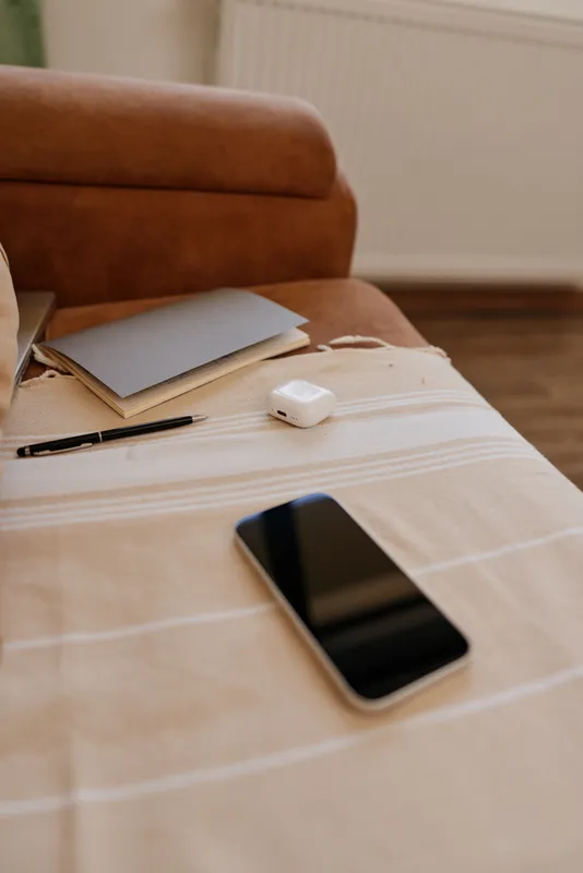 Cozy home living room scene with a smartphone, notebook and pen on a light striped tablecloth beside a soft brown sofa, conveying a quiet focused moment at home for everyday use