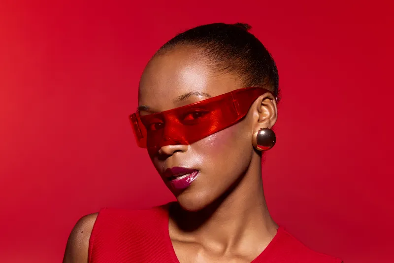 Portrait of a confident black woman with dark skin wearing red futuristic sunglasses and matching red outfit against a red background. Concept for fashion, style, and beauty.