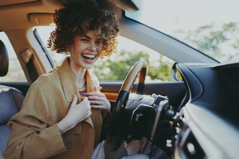 A joyful woman in a car smiles, capturing a candid moment of everyday joy. Retro film color styling highlights warm tones, nostalgia, and casual urban travel.