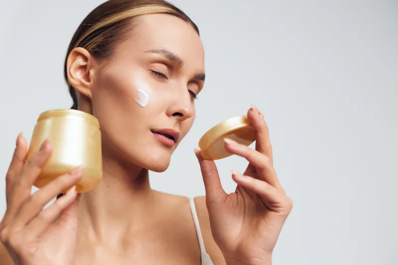 Woman applying face cream, close up on studio background, calm expression, skincare and self care, beauty and wellness, soft light highlights moisturizer texture