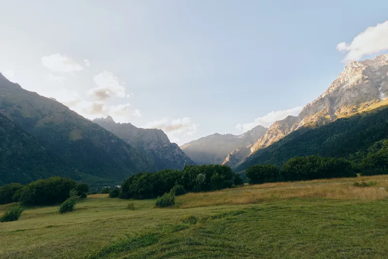Serene mountain valley landscape with lush meadow, distant peaks, and a clear sky, evoking calm, openness and freedom