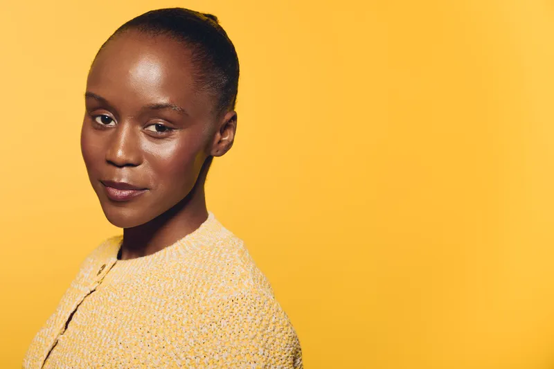 Portrait of confident African woman with dark skin wearing yellow textured top against yellow background. Concept of beauty, fashion, elegance, and self-confidence in studio lighting.