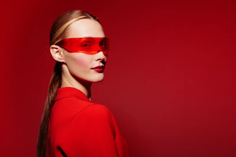 Portrait of a stylish woman wearing red sunglasses and a red jacket against a red background. Concept of fashion, modern style, confidence, and bold color contrast.