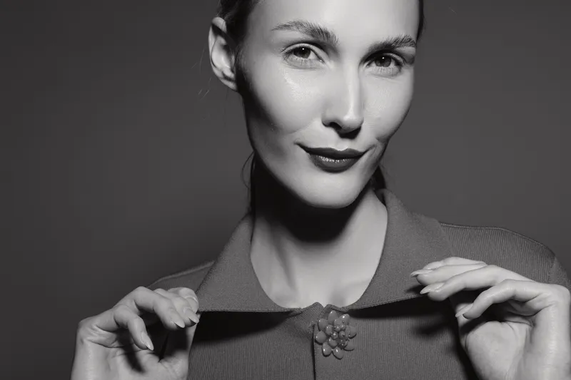 Closeup of a fair skinned Caucasian woman with slicked hair smiling slightly in monochrome studio lighting.