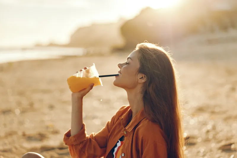 Woman outdoor on beach, sunlight backlit, holding cheese and eating in profile, warm happy summertime mood, relaxed posture, soft breeze, golden sand and ocean waves, smiling gently