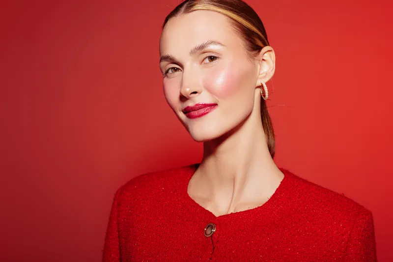 Portrait of confident woman with red lipstick and red sweater on red background. Studio lighting highlights her clear skin and elegant expression. Concept of beauty and fashion.