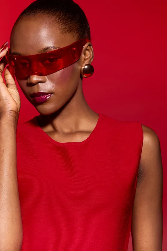 Portrait of a dark skinned African American woman wearing red sunglasses and a red sleeveless top against a red background. Fashion concept with bold colors and modern style.