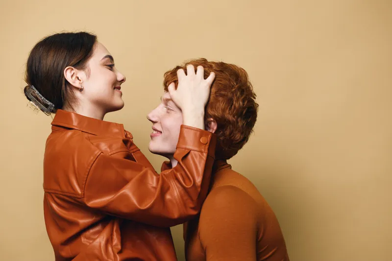 Couple in casual clothes embracing and smiling with happiness and affection for love relationship and warmth on beige background in studio.