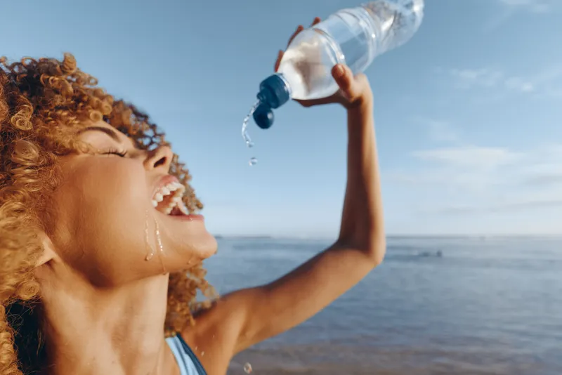 Woman, ocean, water, hydration, summer, bottle, outdoors, drinking, close up profile, woman smiles and drinks, concept refreshment, self care, thirst quenched near sea, blue sky breeze