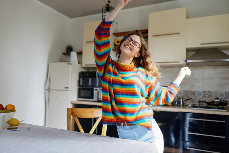 A joyful woman in a striped sweater dances in a bright, modern kitchen, celebrating everyday moments at home.
