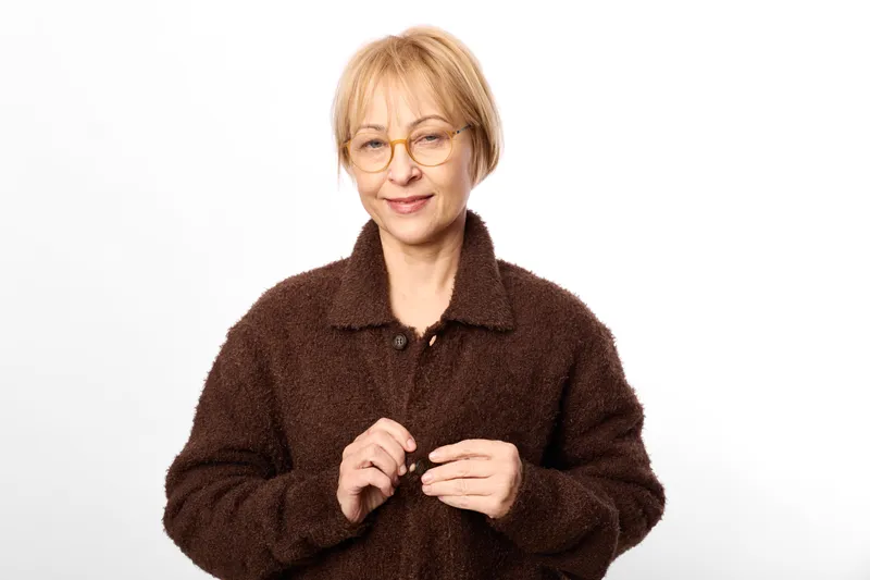Elderly woman with glasses and sweater, smile, hands, portrait on white background, warm casual studio lighting, calm mood, indoor comfort, soft fabric, closeup, fashion