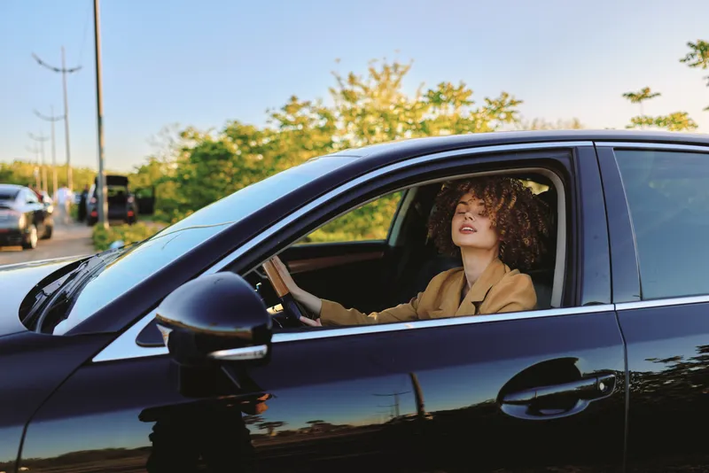 Woman driver sits in a sleek car with retro film color and daylight, capturing a confident lifestyle moment as city streets shimmer through the window and warm cabin light enhances mood