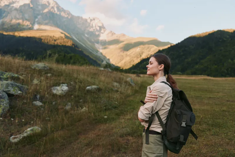Young woman with a backpack enjoys a peaceful moment while hiking in the mountains during a sunny day with clear skies and natural scenery.