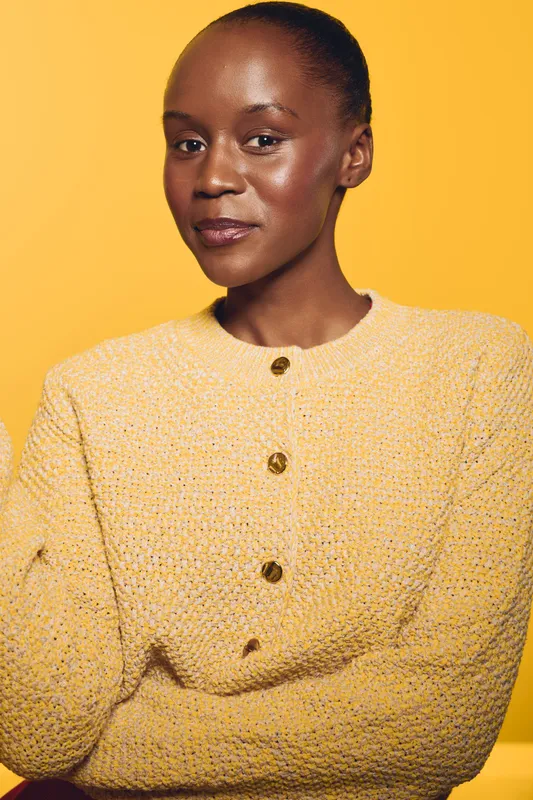 Confident African woman with dark skin wears yellow knitted sweater against yellow background. Studio portrait of elegant female model with natural makeup and serene expression.
