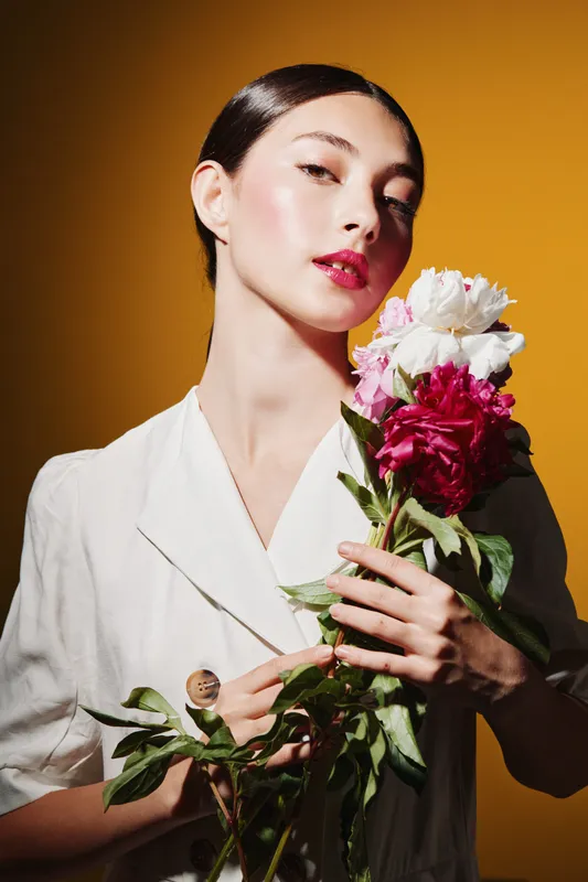 Young woman with glowing makeup poses with bright flowers on an autumn yellow background. Concept for beauty, fashion, and creative cosmetic art in fresh style.